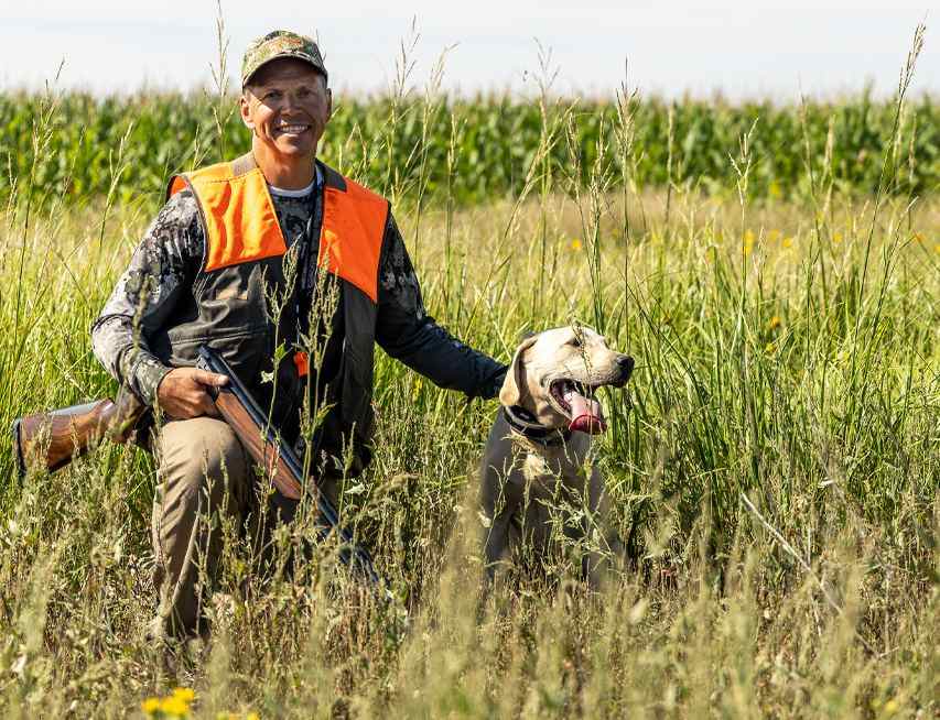 Rapid Rooster guide kneeling in the grass with his yellow Labrador